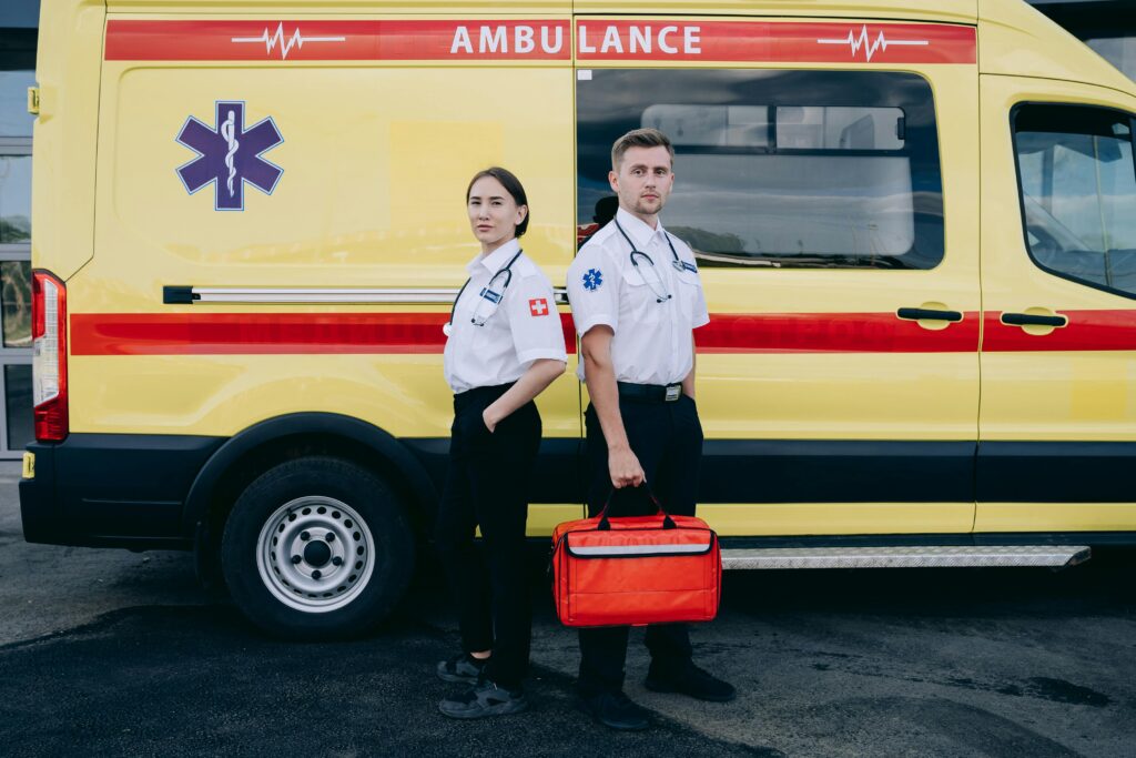 Two paramedics in uniform standing confidently beside a yellow ambulance, ready for emergency response.